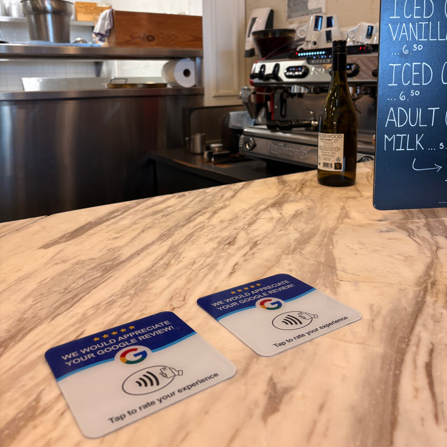 Two 1TapMeta NFC Google review tiles on the marble counter of an Ottawa coffee shop — customers tap their phone to leave a Google review